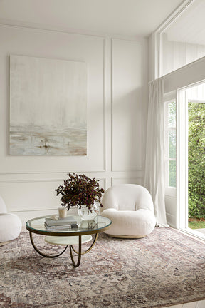 Modern living room with white armchair, glass coffee table, and abstract painting.