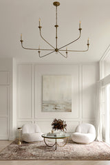 Living room with a chandelier, two white chairs, a coffee table, a painting on the wall & a modern traditional rug.