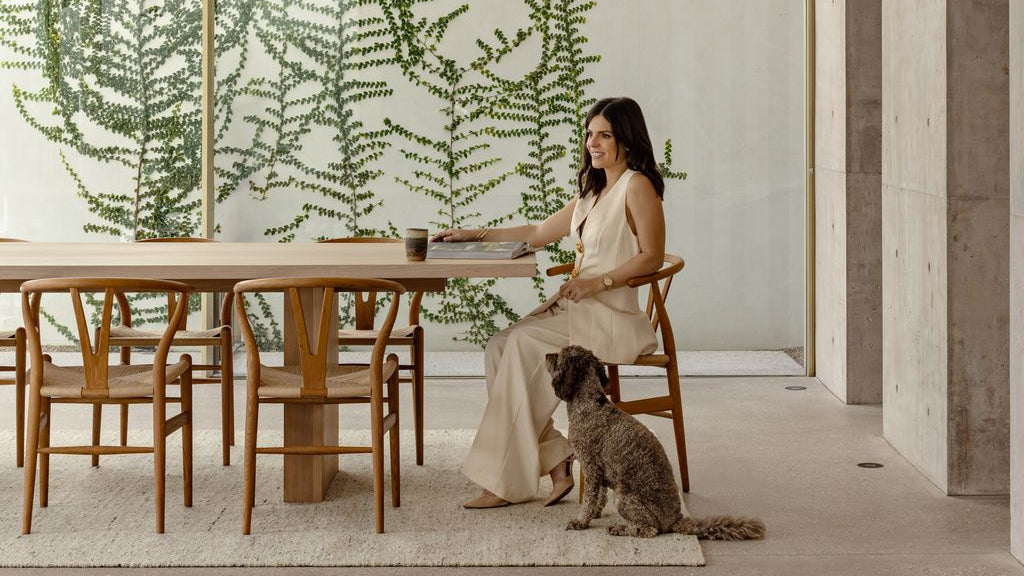Woman sitting at a wooden dining table with a dog in a modern interior setting featuring our Sierra Natural Wool Rug.